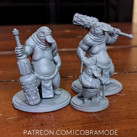 three figurines of fantastical creatures, including a large, muscular creature with a large weapon, a smaller creature with a smaller weapon, and a smaller creature with a smaller weapon.